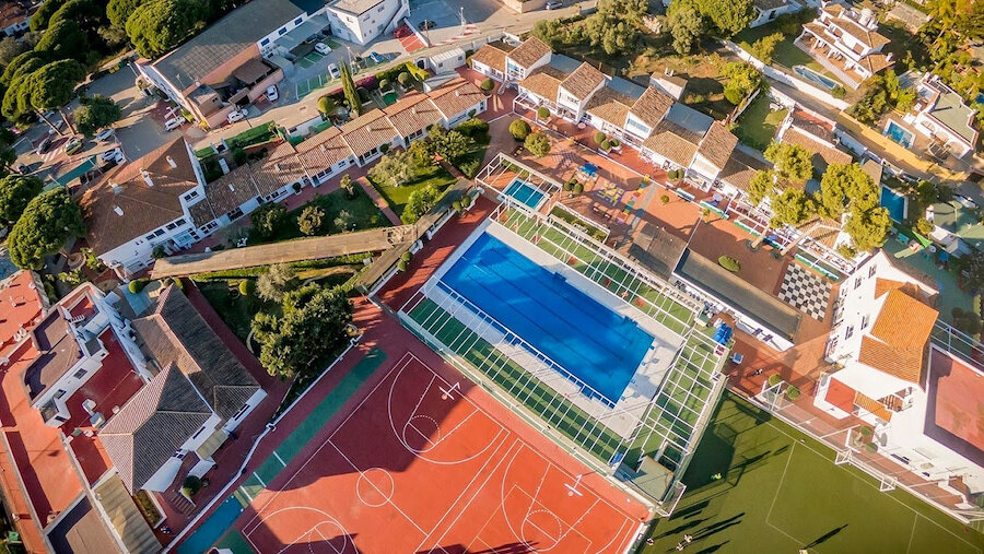 Aerial view of a Marbella school campus featuring a swimming pool, sports courts and outdoor recreation areas
