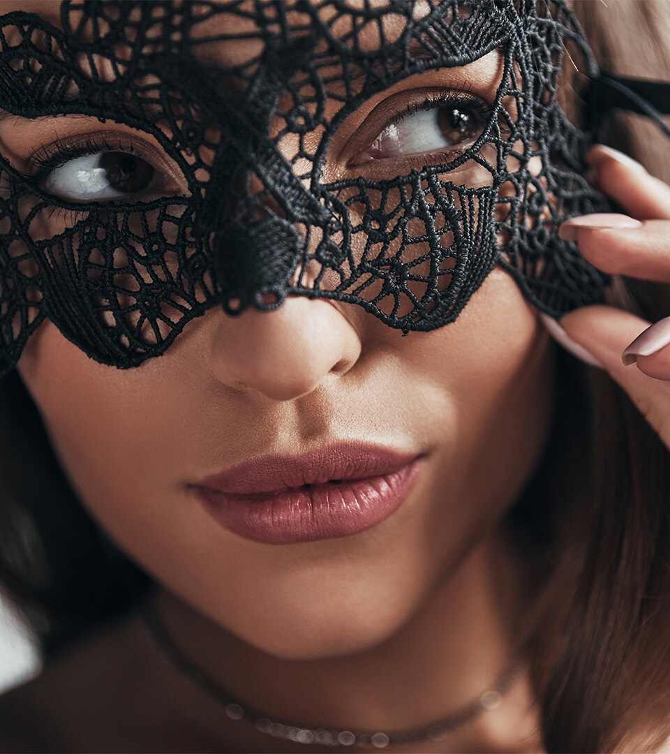 Close-up of a woman adjusting a black lace masquerade mask for Halloween in Marbella.