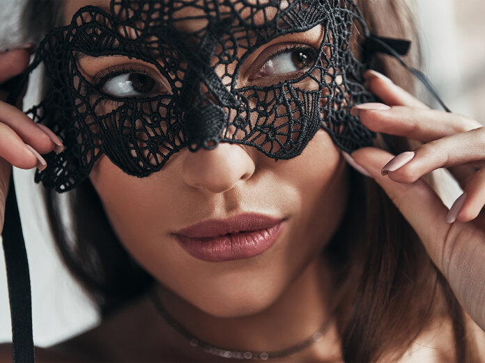 Nahaufnahme einer Frau, die eine schwarze Spitzenmaske für Halloween in Marbella zurechtrückt.