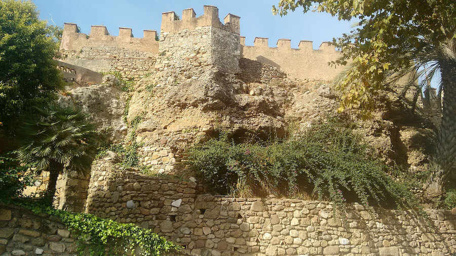 Muros desgastados de una fortaleza y una torre almenada rodeados de vegetación, parte de la historia de Marbella.