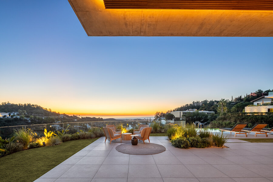 Terras van een eigentijdse villa in El Madroñal, Benahavís, met aangelegde tuinen, buitenzitruimte, zwembadgedeelte en panoramisch zeezicht bij zonsondergang.