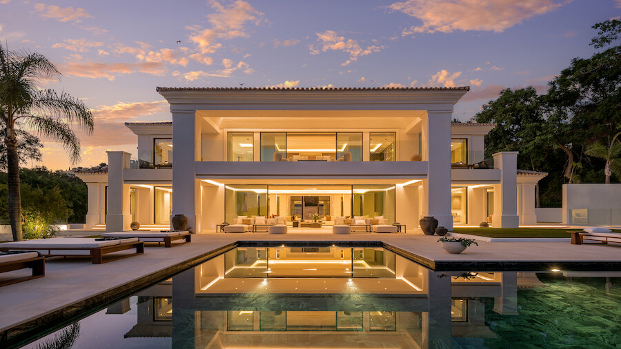 Elegante villa in La Quinta, Benahavís, met verlichte interieurs, aangelegde terrassen en een zwembad dat de woning weerspiegelt in de schemering.