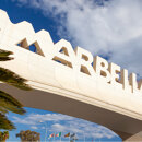 Marbella entrance arch framed by palm trees under a partly cloudy sky