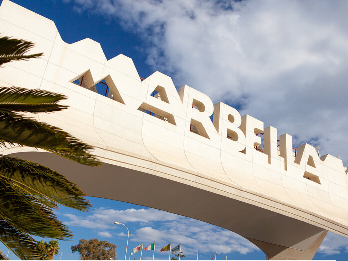 Marbella entrance arch framed by palm trees under a partly cloudy sky