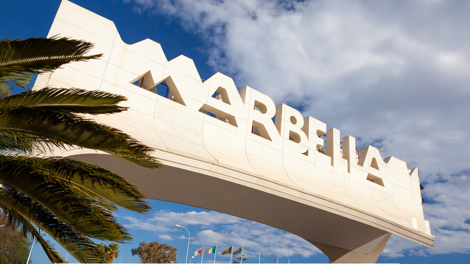 Toegangspoort van Marbella, omringd door palmbomen onder een gedeeltelijk bewolkte hemel