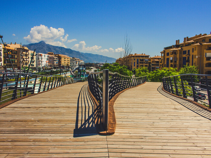 Moderne Fußgängerbrücke über den Boulevard von San Pedro de Alcántara mit dem Berg La Concha im Hintergrund, die den Kontrast zwischen Stadterneuerung und der Geschichte von San Pedro de Alcántara widerspiegelt.