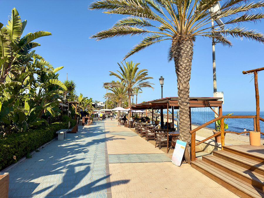 Palm-lined promenade in San Pedro de Alcántara with beachfront restaurants and views of the sea.
