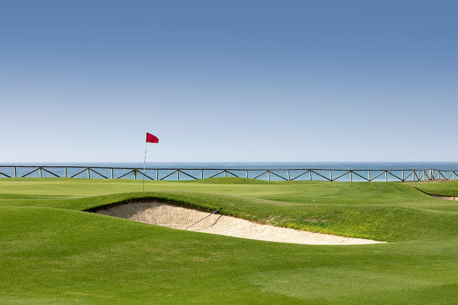 Seaside golf course in San Pedro de Alcántara with a red flag, sand bunker and Mediterranean views.