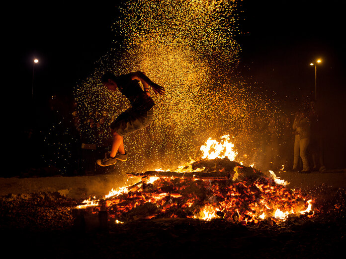 Escena tradicional de salto sobre el fuego con brasas incandescentes y chispas iluminando la Noche de San Juan en Marbella.