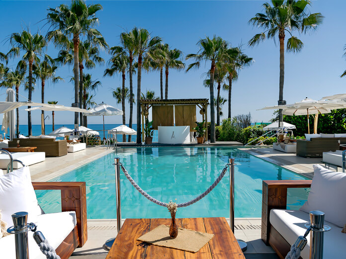 Exclusive beach clubs in Marbella with a pool, white loungers, palm trees and panoramic Mediterranean views