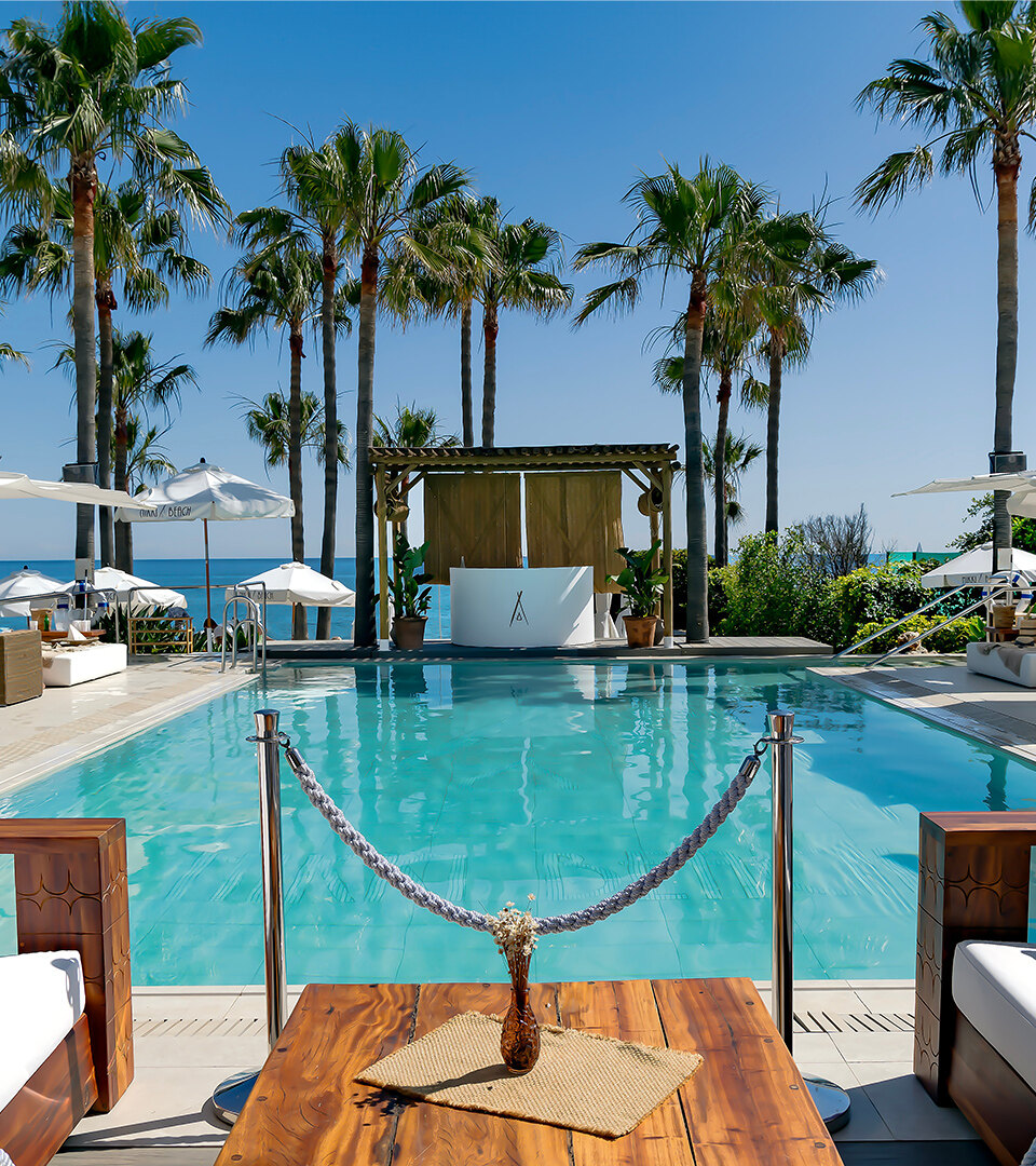 Exclusive beach clubs in Marbella with a pool, white loungers, palm trees and panoramic Mediterranean views