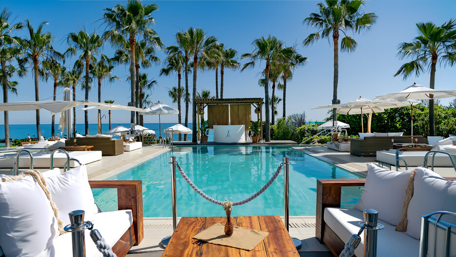 Exclusieve beach clubs in Marbella met zwembad, witte ligbedden, palmbomen en panoramisch uitzicht over de Middellandse Zee