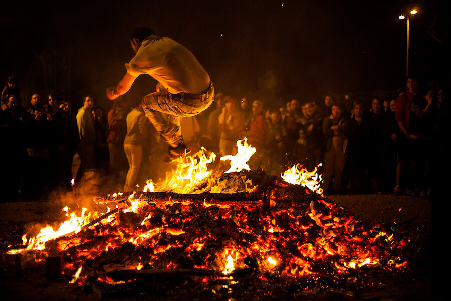 Person jumping over hot embers on the beach at night while a crowd watches the San Juan tradition.