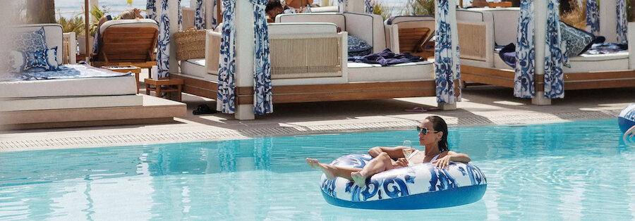 Stylish beach clubs in Marbella with a woman relaxing in the pool beside elegant blue and white cabanas