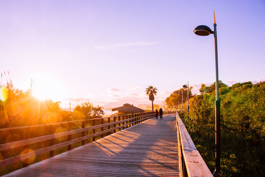 Pasarela de madera con vistas al atardecer que muestra cómo las ciudades para moverse a pie pueden ofrecer preciosos recorridos costeros rodeados de naturaleza y vistas al mar.