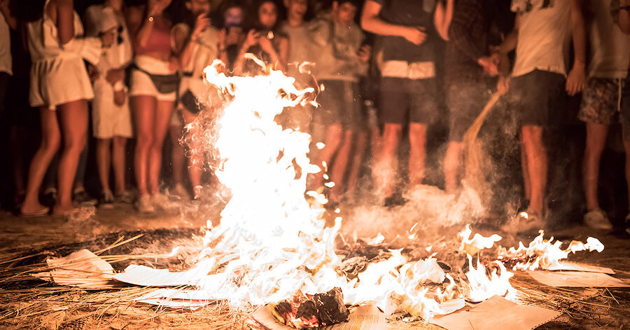 Small beach bonfire surrounded by young people during a lively summer night celebration in Marbella.
