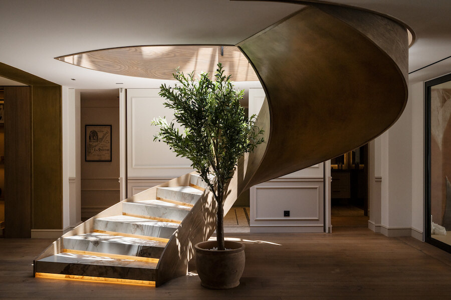 Sculptural staircase with illuminated marble steps and an indoor olive tree in a luxury contemporary home.