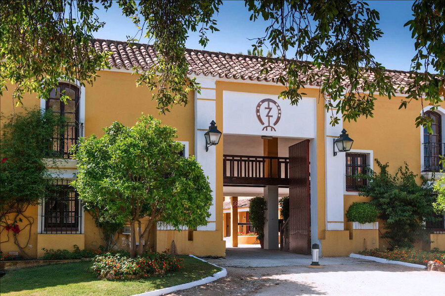 Entrada de un centro ecuestre andaluz para la equitación en Marbella rodeado de jardines y arquitectura tradicional.