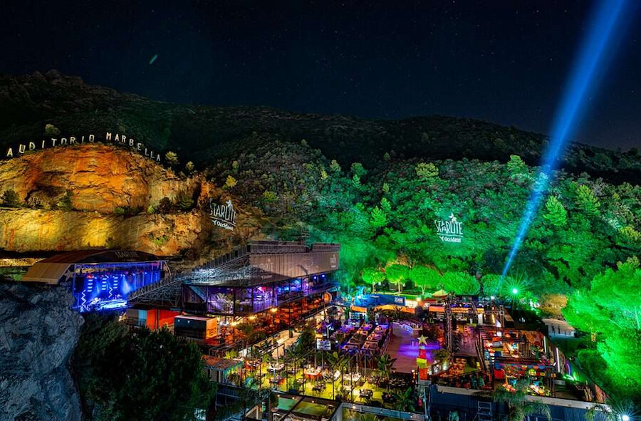The open-air Starlite Marbella 2026 venue illuminated at night, with terraces, stage lights, and mountain views.