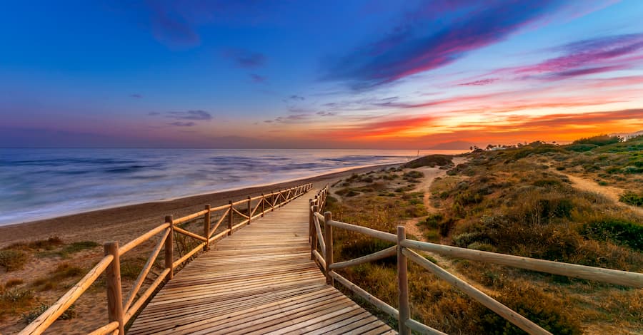 Wooden beach boardwalk through protected dunes on the Marbella East coastline at sunset