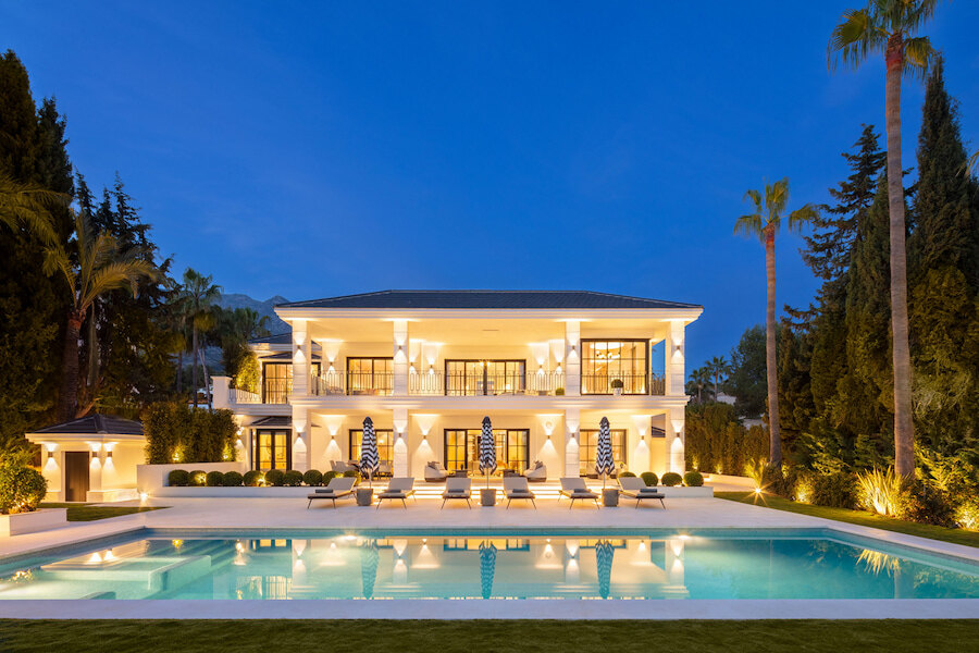 Elegant Mediterranean-style villa at night with a large swimming pool, palm trees and warm exterior lighting