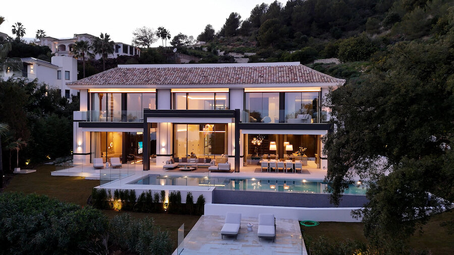 What €10M+ buys on Marbella’s Golden Mile: modern luxury villa at dusk with illuminated interiors, pool and landscaped gardens