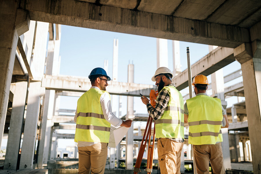 Construction professionals in safety helmets and high-visibility vests inspecting a building site structure.