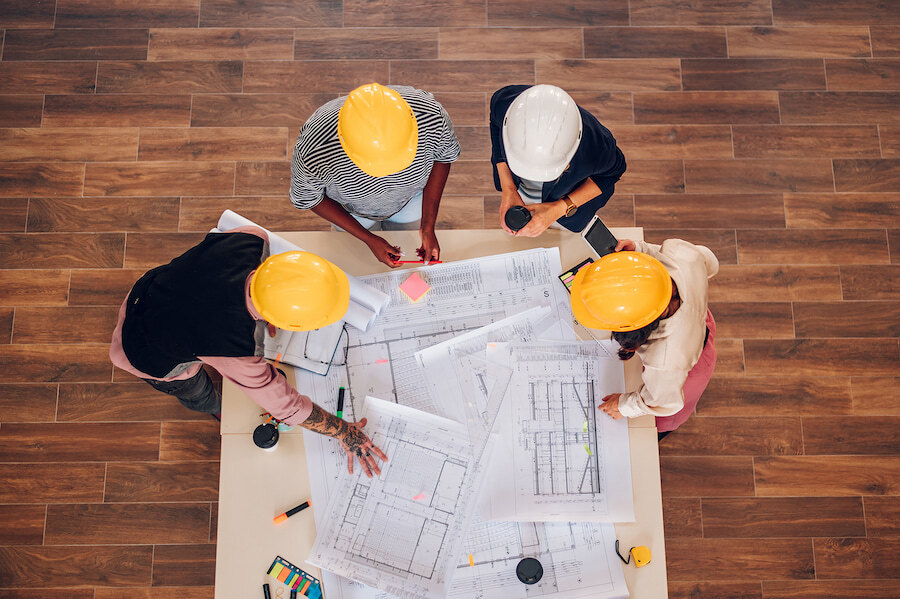 off-plan in Marbella. Overhead view of four construction professionals in hard hats reviewing architectural plans around a table.