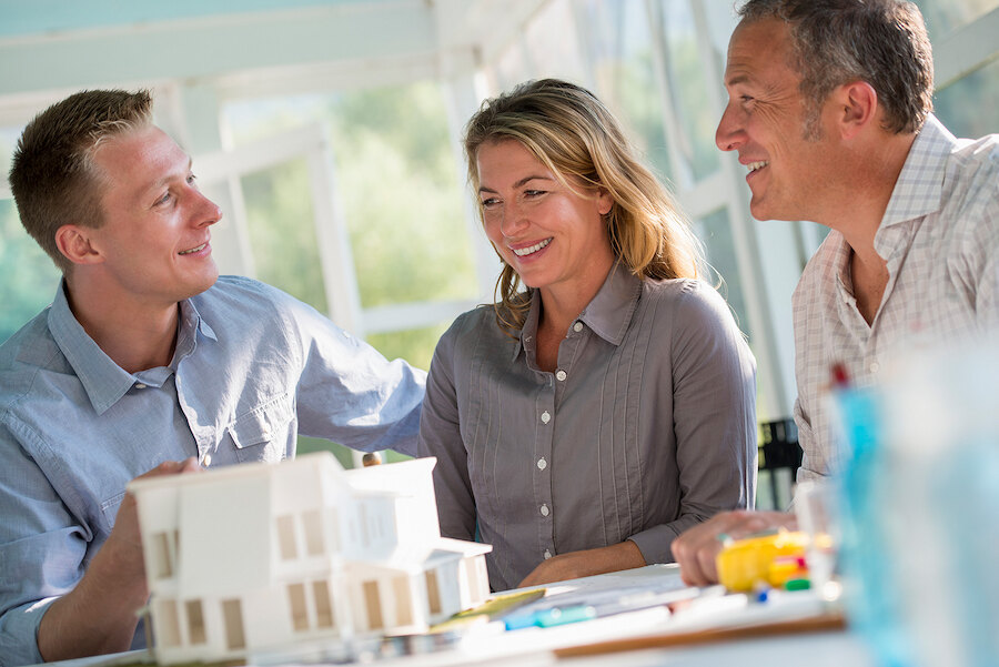 Three people smiling during a property consultation, seated at a table with a scale model of a modern house.