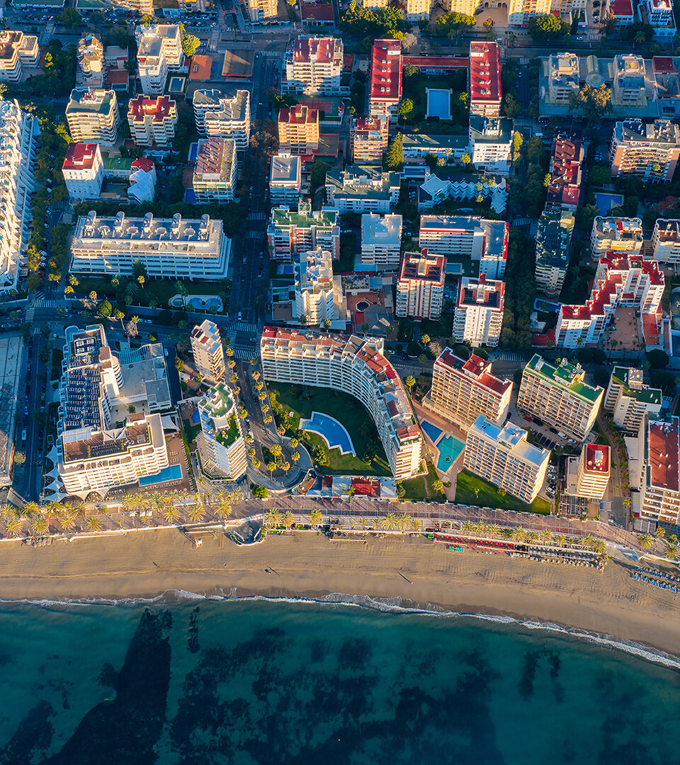 Vue aérienne du front de mer de Marbella, montrant des immeubles d’appartements en bord de mer, la promenade, la plage de sable et la mer Méditerranée.