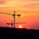 Grúas de construcción recortadas sobre un intenso atardecer naranja, con el sol bajo en el horizonte sobre un atardecer.