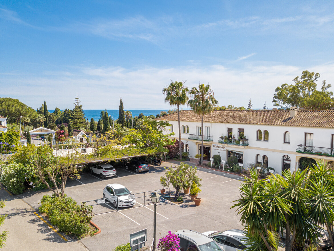 Vue aérienne des bureaux de Panorama à Marbella, entourés de palmiers et de jardins, avec la mer Méditerranée en arrière-plan.