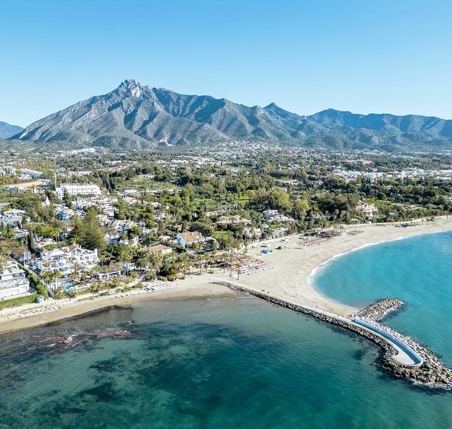 Luftpanorama eines Strandes in Marbella mit Yachthafen, türkisfarbenem Mittelmeer und dem Berg La Concha über der Küste.