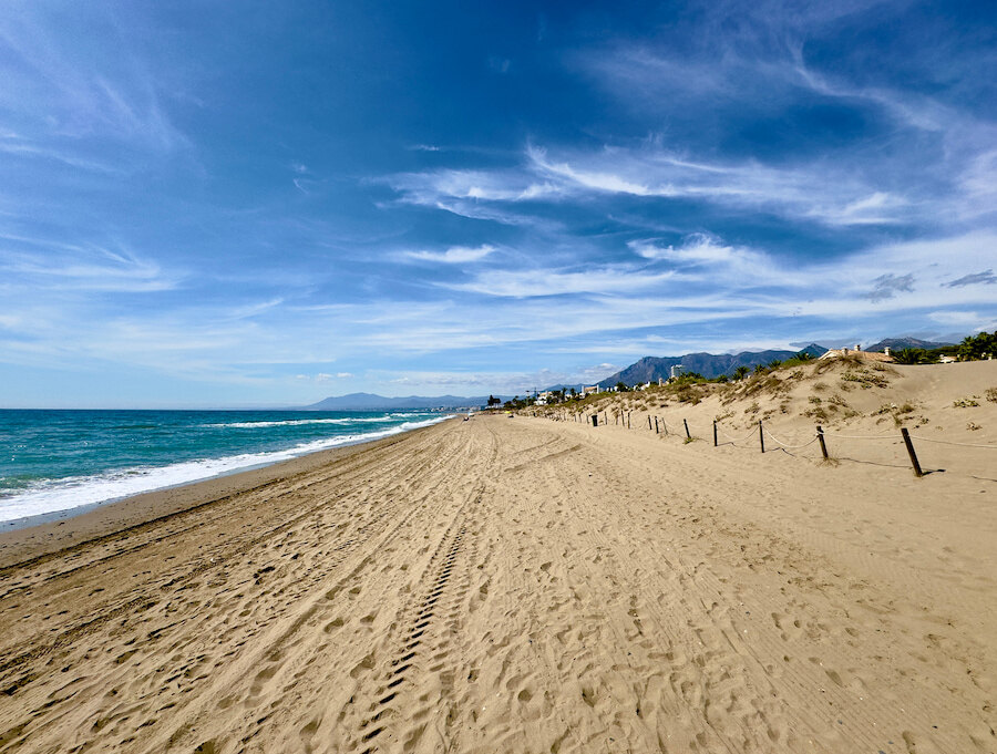 Langer Sandstrand in Marbella mit Dünen, ruhigen Wellen und malerischem Bergblick entlang der Costa del Sol.