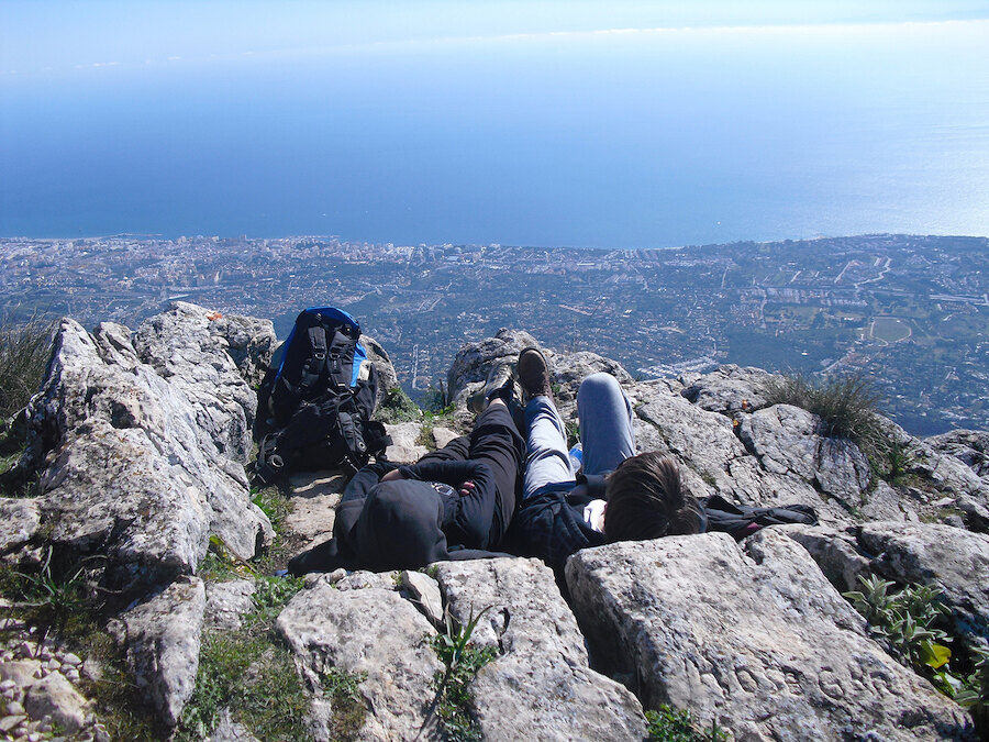 Twee wandelaars rusten tussen de rotsen terwijl ze genieten van een weids uitzicht over Marbella en de zee.