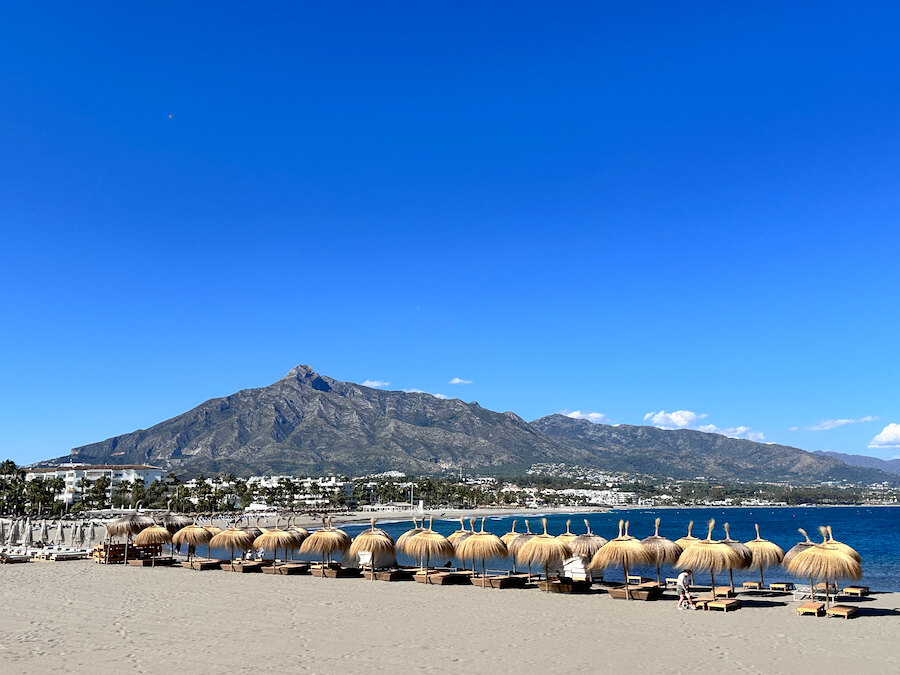 Einer der besten Strände in Marbella mit goldenem Sand, traditionellen Sonnenschirmen, klarem blauem Wasser und Blick auf den Berg La Concha.