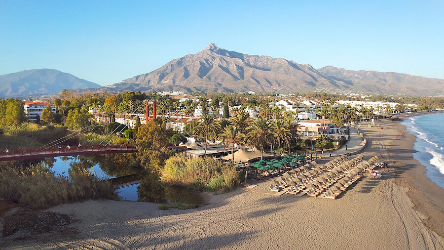 Badplaats met palmbomen langs het strand en La Concha Marbella als indrukwekkende achtergrond.