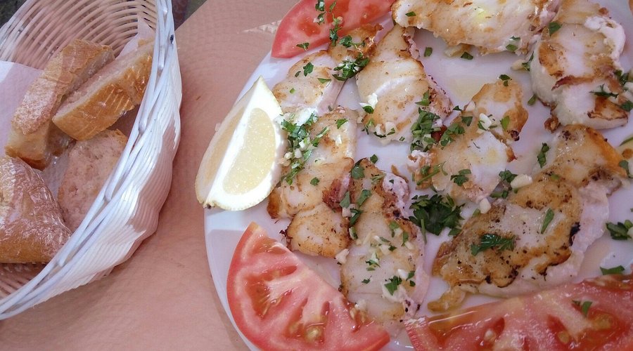 Plate of grilled fish with garlic, parsley, lemon, and tomato, served with bread at a Marbella restaurant.