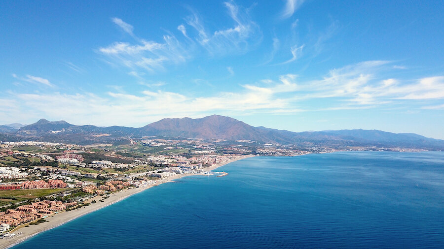 Panoramic aerial view of Málaga’s coastline with long beaches, residential areas, and mountains beside the Mediterranean.