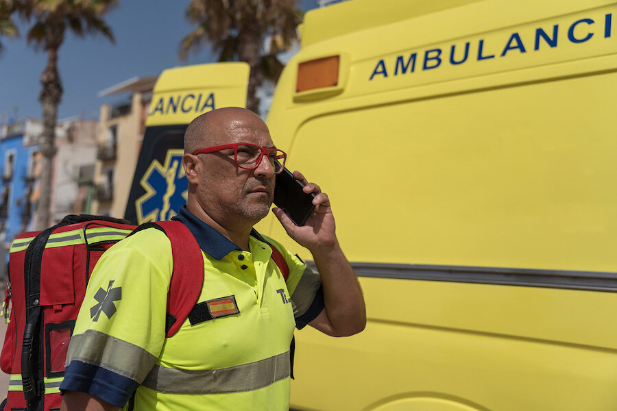 public healthcare. Paramedic talking on the phone beside an ambulance, wearing a high-visibility uniform and medical backpack.