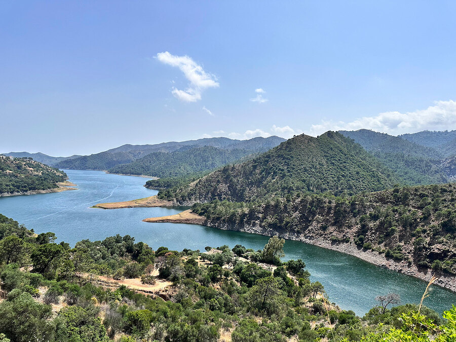 spring hikes. Scenic view of a winding lake surrounded by green hills and rugged mountains under a clear blue sky near Marbella.