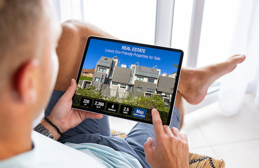 Man browsing luxury eco-friendly properties for sale on a tablet while relaxing at home.