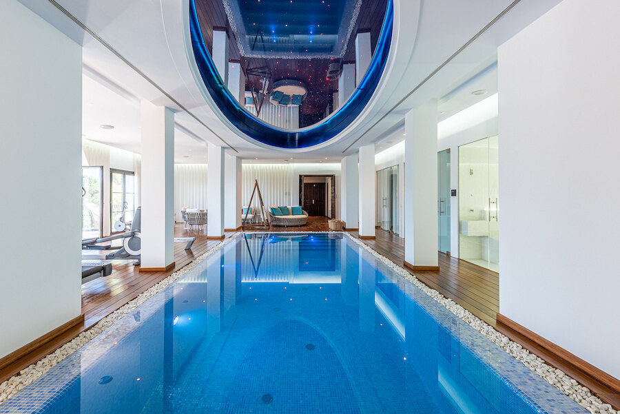 Large indoor swimming pool with blue ceiling lighting in one of the top villas in Marbella with spa