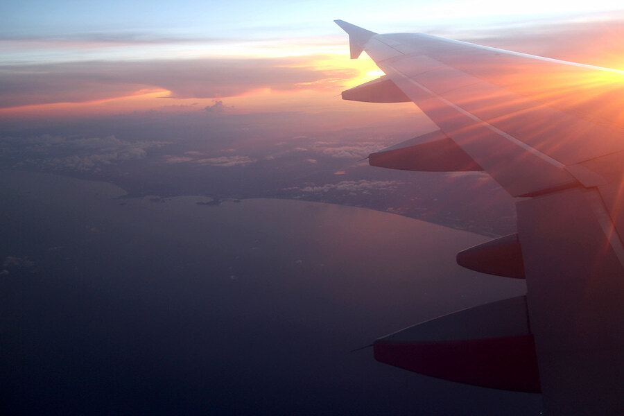 Vista desde la ventanilla de un avión al atardecer, con el ala sobre la línea de costa, simbolizando la facilidad de los viajes internacionales y la accesibilidad global de Marbella.