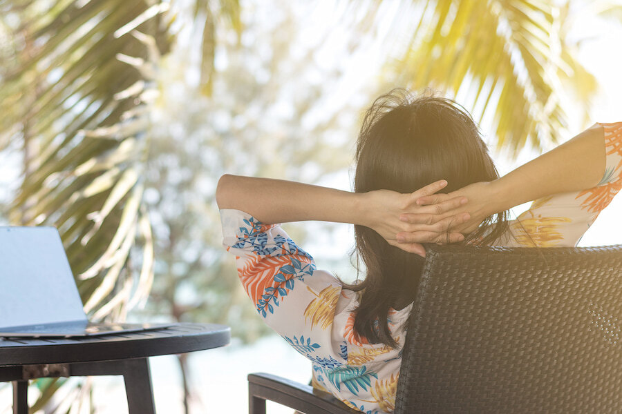 Mujer relajándose en una terraza soleada junto a un portátil y palmeras, reflejando el equilibrio de Marbella entre el teletrabajo y el estilo de vida al aire libre.