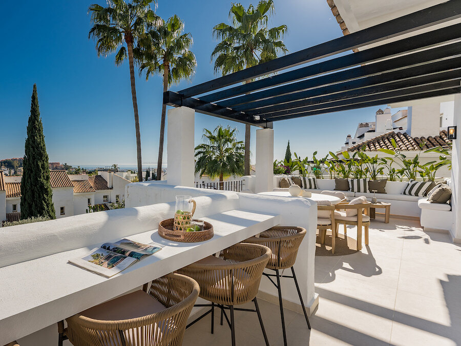 Bright luxury terrace with outdoor lounge, dining area, palm trees and partial sea views in Marbella.