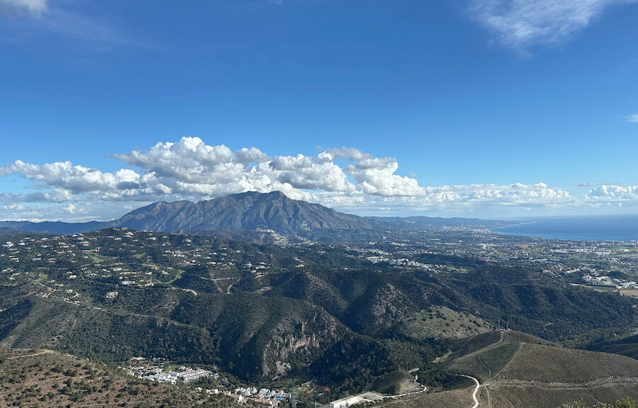Sweeping view of La Concha mountain, Marbella’s rolling hills and the Mediterranean coastline beneath a bright blue sky with scattered clouds.