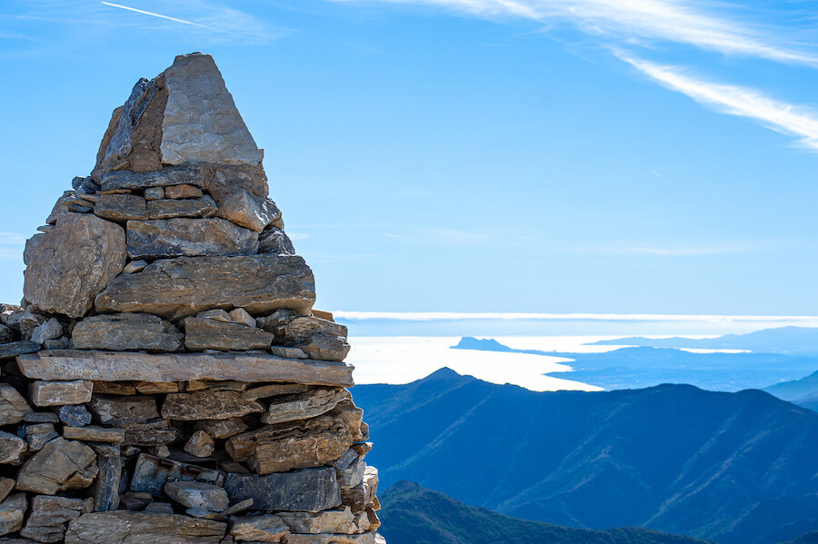 Stone summit marker overlooking layered mountain ridges and a shimmering coastal horizon under a clear blue sky near Marbella.