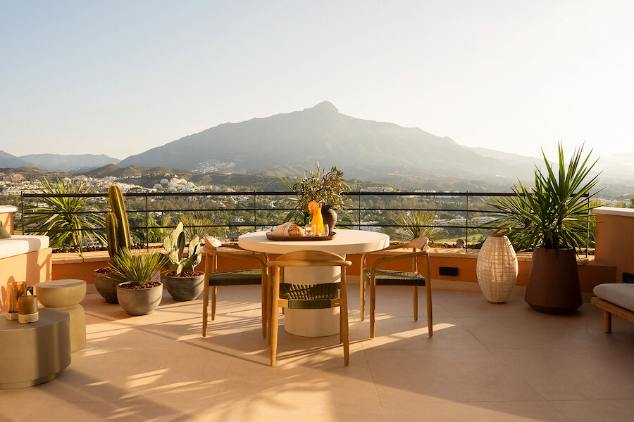 Sunlit terrace of a duplex penthouse in Magna Marbella with outdoor dining area, decorative plants and panoramic mountain views.