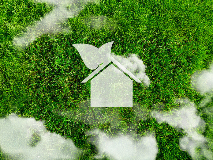 Aerial view of Europe formed in green grass, with a white eco-friendly house icon and soft clouds above, symbolising sustainable real estate and green housing.
